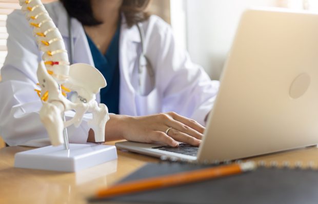close up physical therapist type on laptop to search about patient's record with human skeleton anatomy at room for advice and consult of treatment for healthcare and telemedicine concept